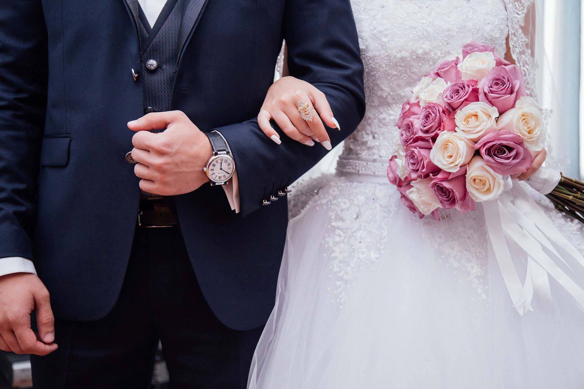 Hochzeitspaar schreitet voran und hält sich im Arm mit Blumen